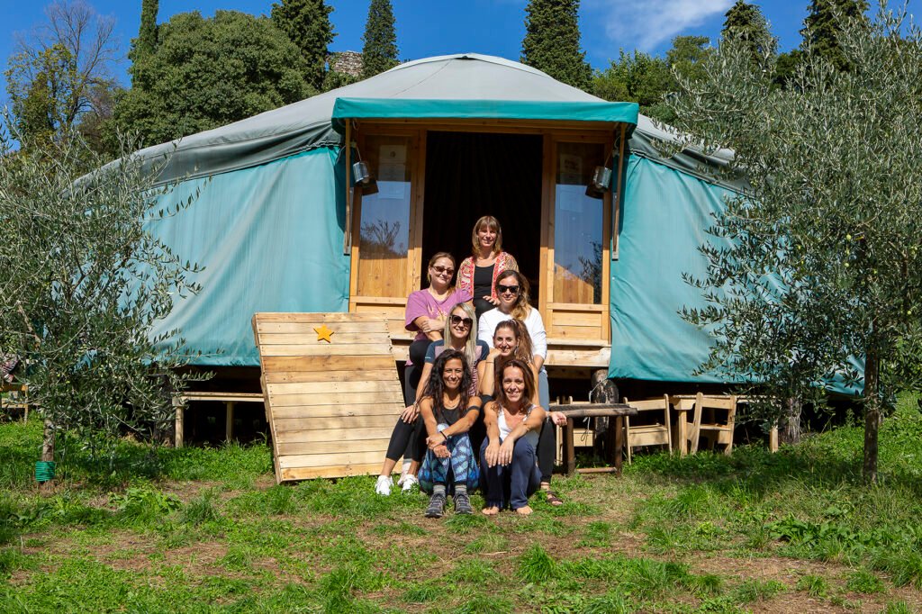 Group of people sitting outdoors in front of a teal yurt during a somatic release retreat in nature.