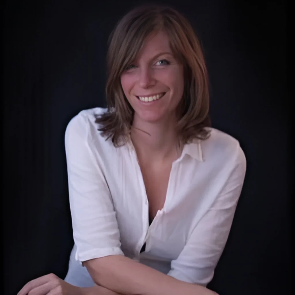 Professional portrait of Nastassja Ugolini smiling, wearing a white shirt against a dark background